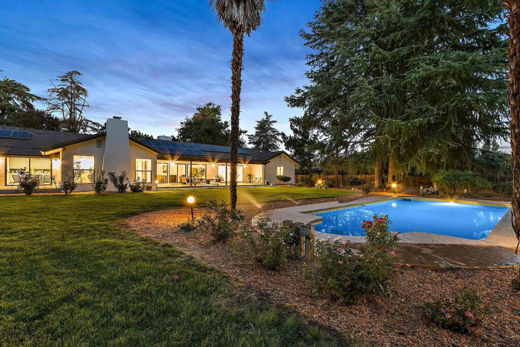 A serene home with a sparkling pool and well-maintained lawn, set against the backdrop of a dusky sky.