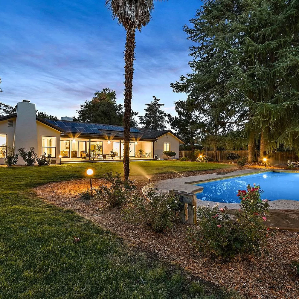 A serene home with a sparkling pool and well-maintained lawn, set against the backdrop of a dusky sky.